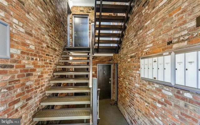 staircase featuring a high ceiling, brick wall, and a mail area