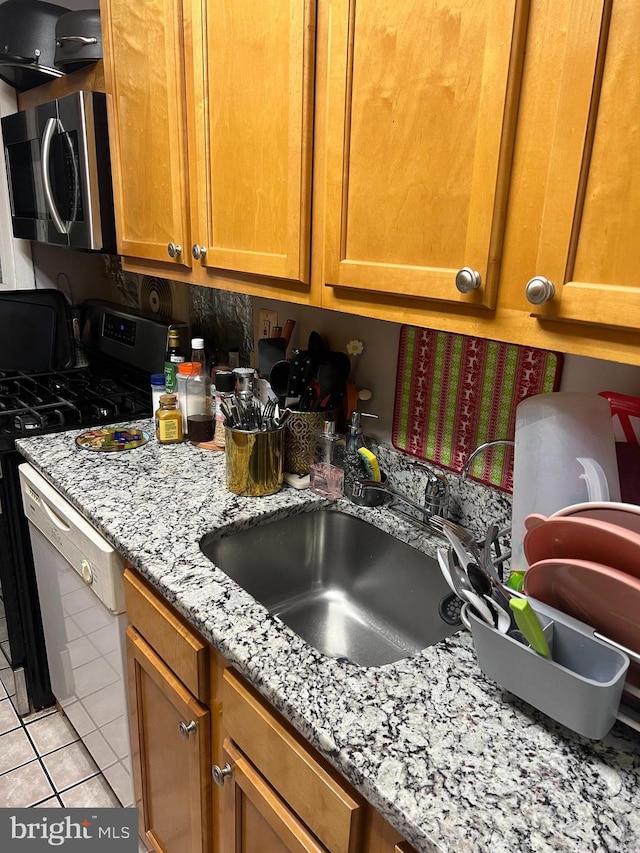 kitchen with sink, stove, light tile patterned floors, light stone counters, and white dishwasher