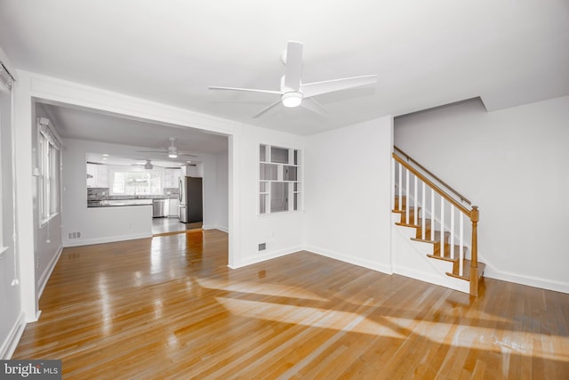 unfurnished living room with baseboards, ceiling fan, stairway, and wood finished floors