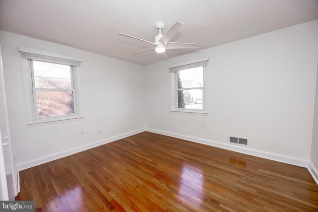 unfurnished room with a healthy amount of sunlight, baseboards, visible vents, and dark wood-type flooring