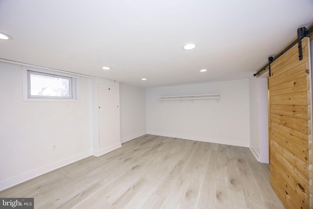 below grade area featuring light wood-type flooring, a barn door, baseboards, and recessed lighting