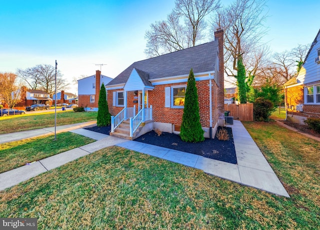 bungalow-style home with driveway, brick siding, a chimney, fence, and a front yard