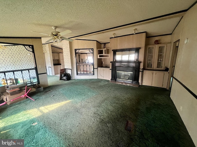 unfurnished living room featuring a healthy amount of sunlight, ceiling fan, dark carpet, and a textured ceiling