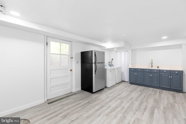 kitchen with stainless steel refrigerator, washer and clothes dryer, sink, and light wood-type flooring