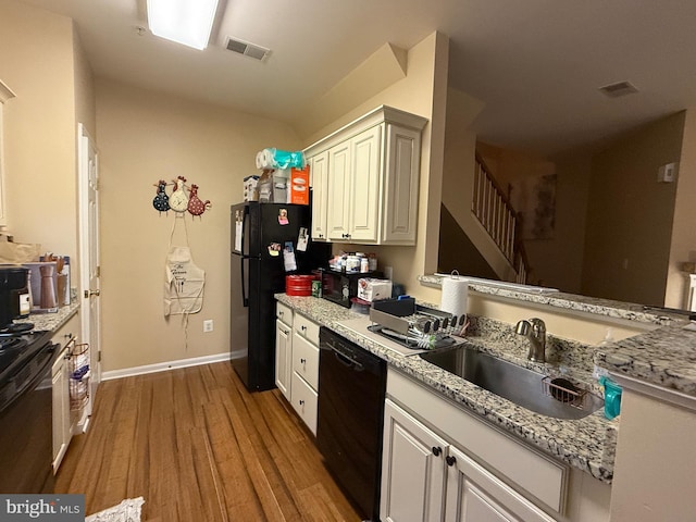 kitchen featuring light stone counters, light hardwood / wood-style floors, sink, and black appliances