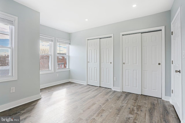 unfurnished bedroom featuring multiple closets and light hardwood / wood-style floors