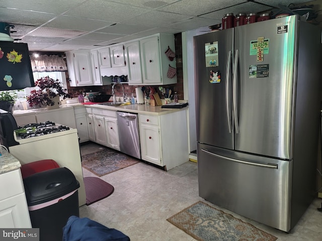 kitchen with stainless steel appliances, white cabinetry, sink, and a paneled ceiling