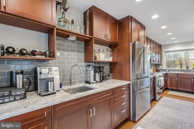 kitchen with sink, appliances with stainless steel finishes, light stone countertops, light hardwood / wood-style floors, and decorative backsplash