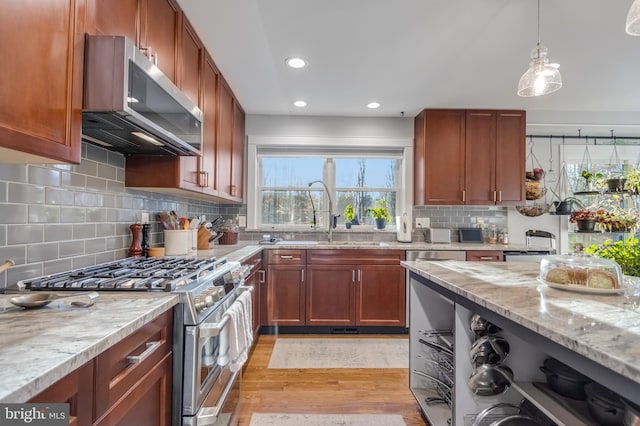 kitchen with stainless steel appliances, light stone counters, decorative backsplash, decorative light fixtures, and light wood-type flooring