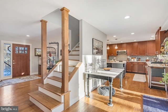 kitchen featuring stainless steel appliances, decorative backsplash, decorative light fixtures, light wood-type flooring, and ornate columns