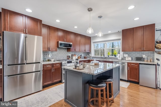 kitchen featuring a kitchen island, appliances with stainless steel finishes, decorative light fixtures, light hardwood / wood-style floors, and light stone counters