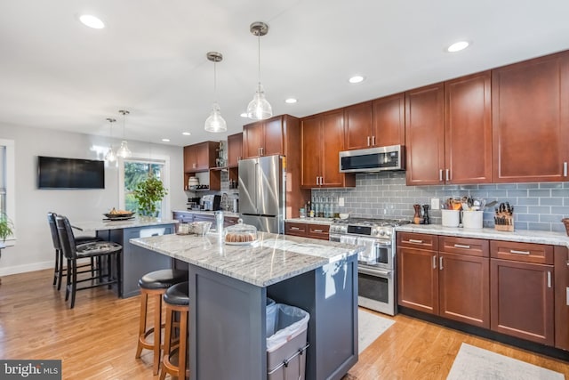 kitchen featuring hanging light fixtures, appliances with stainless steel finishes, an island with sink, light stone countertops, and light hardwood / wood-style floors