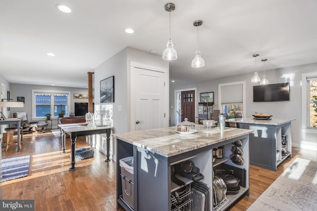 kitchen featuring pendant lighting, dark hardwood / wood-style flooring, a center island, and light stone countertops