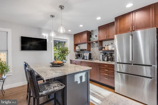 kitchen featuring sink, light hardwood / wood-style flooring, stainless steel refrigerator, a kitchen breakfast bar, and light stone countertops