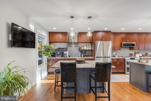 kitchen with hanging light fixtures, appliances with stainless steel finishes, light stone countertops, light hardwood / wood-style floors, and decorative backsplash