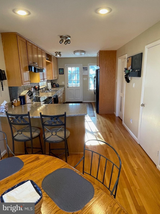 kitchen with black fridge, range, a kitchen breakfast bar, kitchen peninsula, and light hardwood / wood-style floors