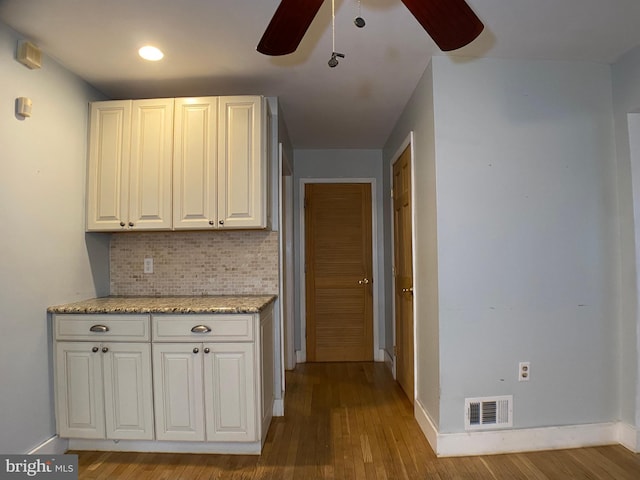 kitchen featuring ceiling fan, white cabinetry, backsplash, light stone countertops, and light wood-type flooring