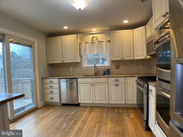 kitchen featuring appliances with stainless steel finishes, stone countertops, sink, white cabinets, and light wood-type flooring