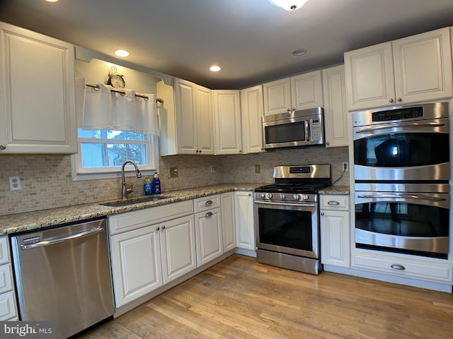 kitchen with appliances with stainless steel finishes, sink, white cabinets, light stone countertops, and light hardwood / wood-style flooring