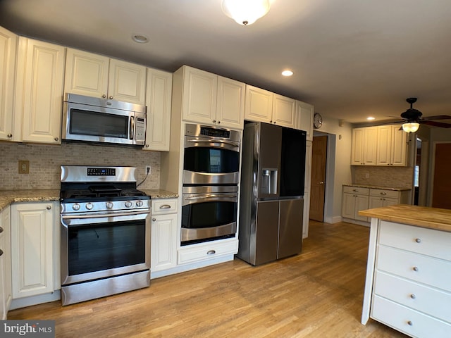 kitchen featuring stainless steel appliances, light stone countertops, light hardwood / wood-style floors, white cabinets, and decorative backsplash