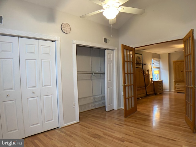 unfurnished bedroom with ceiling fan, light hardwood / wood-style flooring, multiple closets, and vaulted ceiling