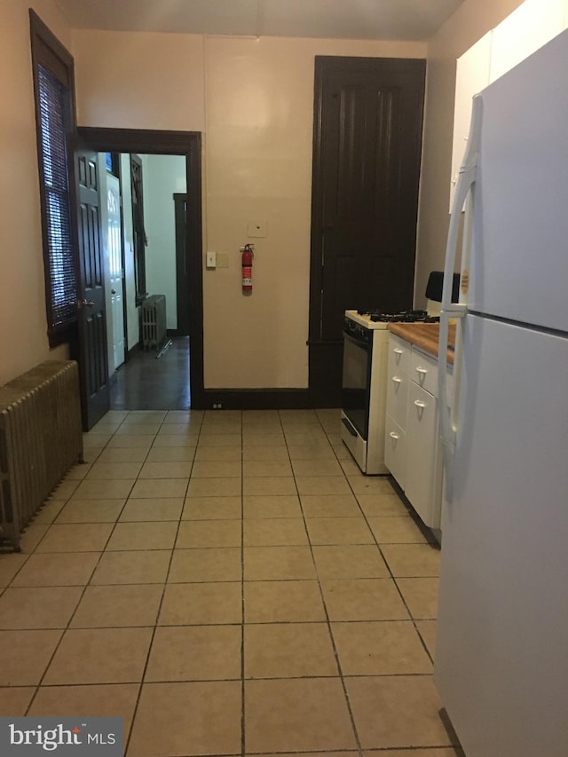 kitchen featuring light tile patterned flooring, white cabinetry, radiator heating unit, white fridge, and gas range oven