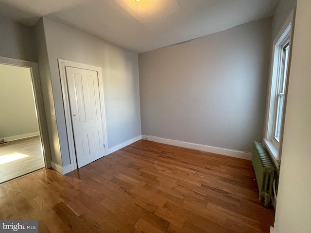 unfurnished bedroom with multiple windows, radiator, hardwood / wood-style floors, and a closet