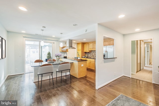 kitchen with range hood, stainless steel fridge, hanging light fixtures, hardwood / wood-style flooring, and kitchen peninsula