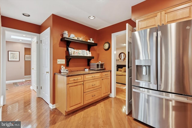 kitchen with light brown cabinetry, stainless steel fridge with ice dispenser, dark stone counters, and light wood-type flooring