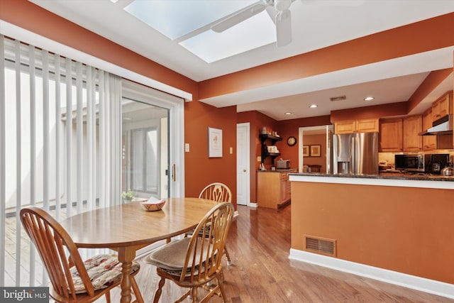 dining space with a skylight, light hardwood / wood-style floors, and ceiling fan