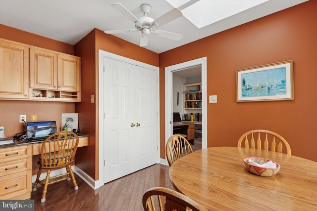 dining room featuring a skylight, built in desk, dark hardwood / wood-style floors, and ceiling fan