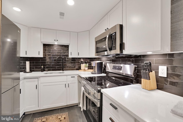 kitchen featuring stainless steel appliances, backsplash, a sink, and white cabinetry