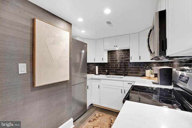 kitchen featuring stainless steel appliances, light countertops, decorative backsplash, white cabinetry, and a sink