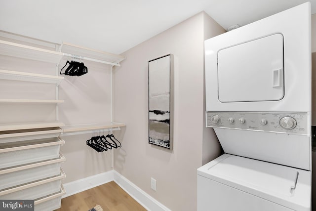 laundry room with light wood-type flooring, stacked washer / dryer, and baseboards