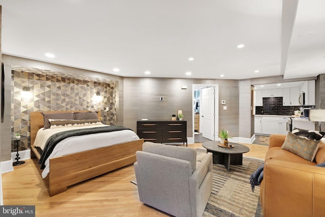 bedroom featuring baseboards, light wood-type flooring, a sink, and recessed lighting