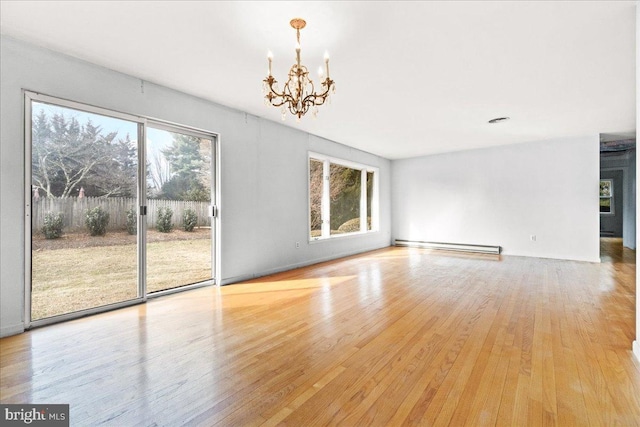 unfurnished living room featuring a baseboard heating unit, a wealth of natural light, light wood-style flooring, and an inviting chandelier