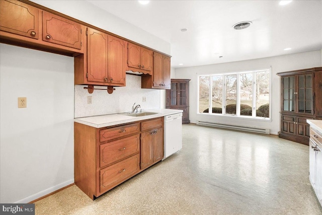 kitchen with brown cabinetry, dishwasher, baseboard heating, light countertops, and a sink