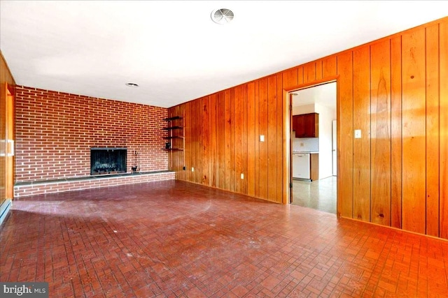 unfurnished living room with a brick fireplace, visible vents, wooden walls, and brick patterned floor