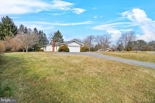 view of front of property featuring a garage, a chimney, a front lawn, and aphalt driveway