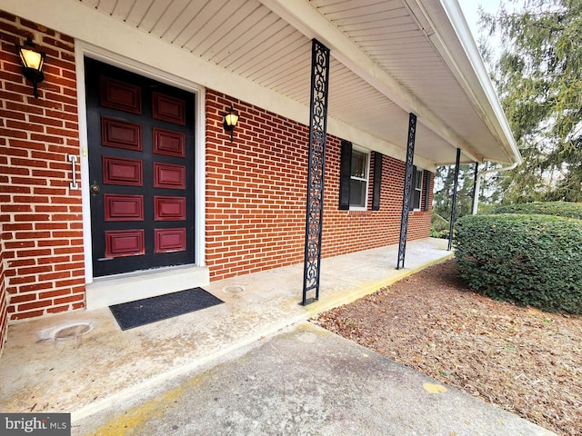 view of exterior entry with a porch, brick siding, and a garage