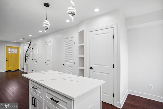 kitchen with hanging light fixtures, light stone countertops, dark wood-type flooring, and white cabinets