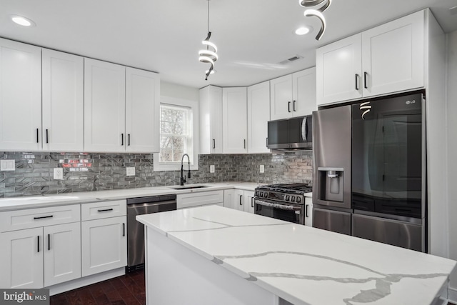 kitchen featuring appliances with stainless steel finishes, sink, white cabinets, hanging light fixtures, and light stone countertops