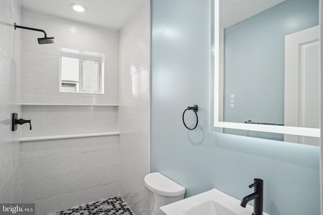 bathroom featuring tiled shower, toilet, and sink