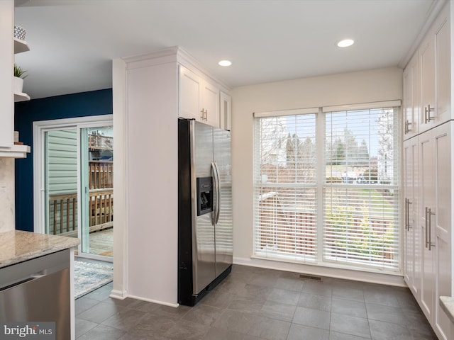 kitchen with white cabinetry, stainless steel appliances, light stone countertops, and dark tile patterned flooring