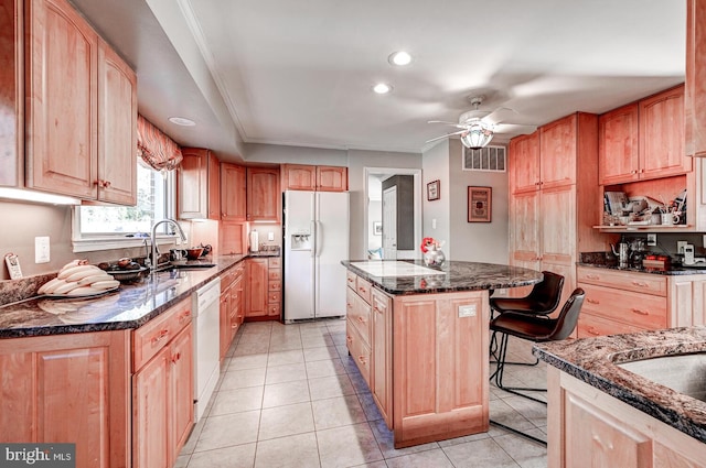 kitchen featuring sink, a breakfast bar area, dark stone countertops, a kitchen island, and white appliances