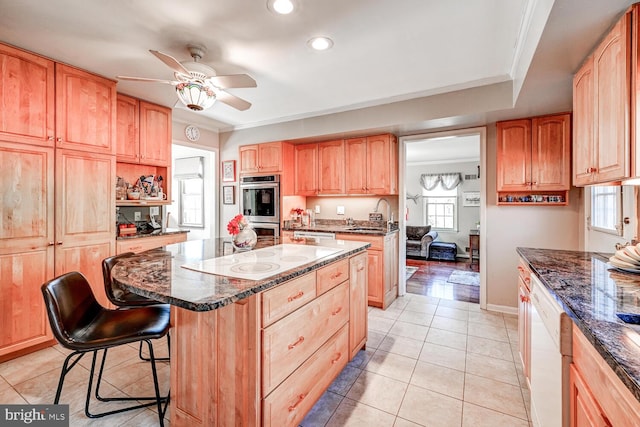 kitchen with white appliances, a kitchen breakfast bar, a center island, ornamental molding, and dark stone counters