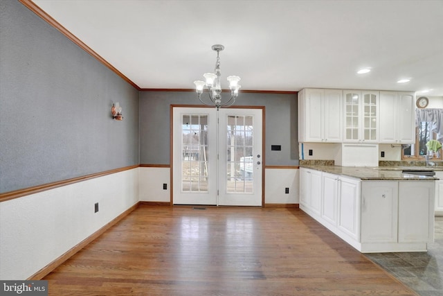 kitchen featuring white cabinetry, hanging light fixtures, dark stone countertops, kitchen peninsula, and light wood-type flooring