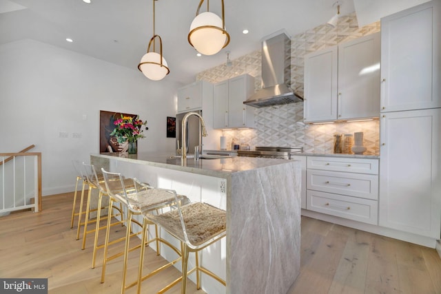 kitchen featuring a breakfast bar, pendant lighting, sink, a kitchen island with sink, and wall chimney range hood