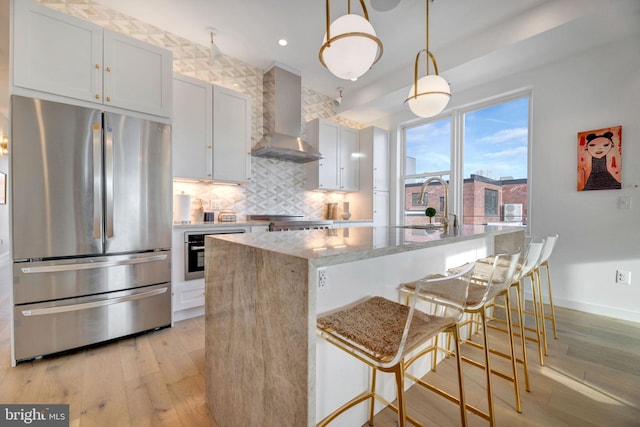 kitchen with stainless steel appliances, a center island, white cabinets, decorative light fixtures, and wall chimney exhaust hood