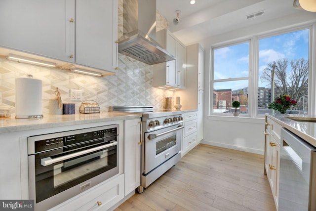 kitchen featuring extractor fan, light wood-type flooring, white cabinets, stainless steel appliances, and backsplash